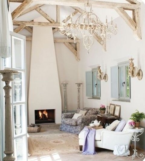 a beautiful Provence living room with a refined chandelier, chic furniture and a fireplace plus shutters and wall sconces