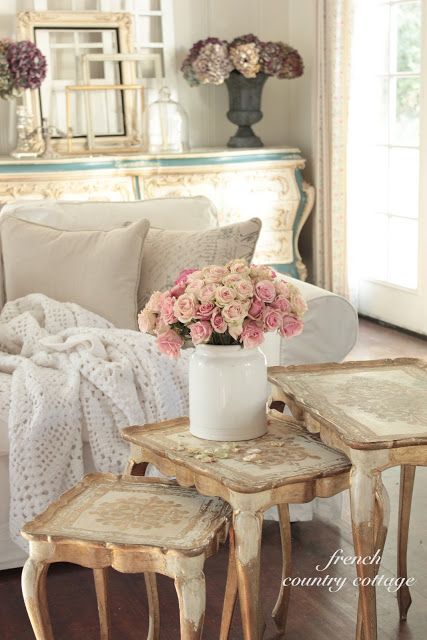 a neutral shabby chic Provence living room with a white sofa, a stack of refined stools and frames plus pastel blooms