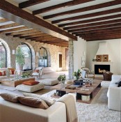 a contemporary Provence living room with a fireplace, neutral furniture, wooden beams and stone walls