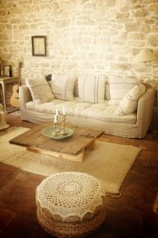 a farmhouse Provence living room with stone walls, pretty neutral furniture, a low wooden table and jute poufs