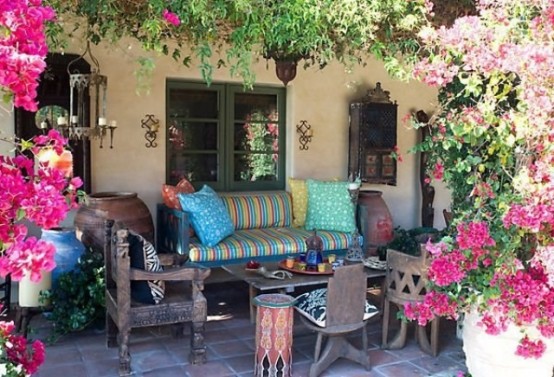 a Moroccan boho terrace with plenty of color, with dark-stained carved furniture, colorful pillows and upholstery, greenery and bold flowers