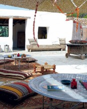 a Moroccan terrace with Moroccan rugs, wooden stools and a bench, bright upholstery, round hammered tables