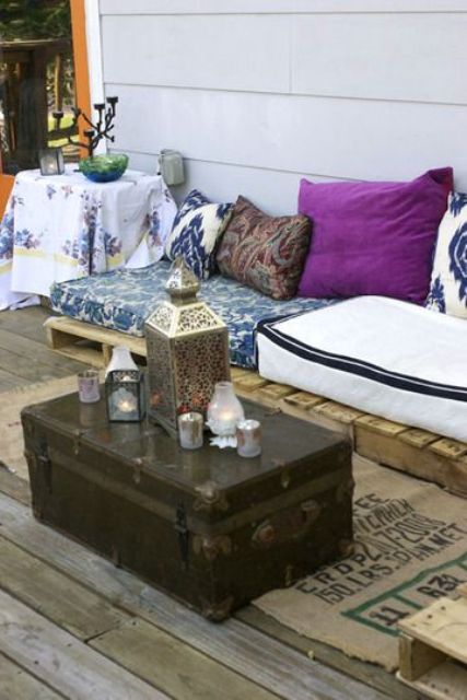 a small boho nook with a deck, low wooden furniture, colorful pillows and upholstery, a chest as a coffee table and Moroccan candle lanterns