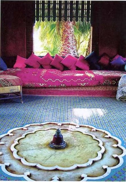 a colorful Moroccan terrace with a blue mosaic wall, a sofa with bold fuchsia upholstery and pillows, chairs with bright covers