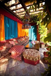 a colorful Morocco-style boho terrace with turquoise and orange curtains, soft seating furniture with bright upholstery, potted greenery