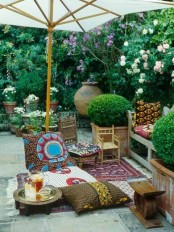 a colorufl boho nook under an umbrella, with a pallet sofa with bright upholstery and pillows, a rug and pillows, potted greenery and bowls