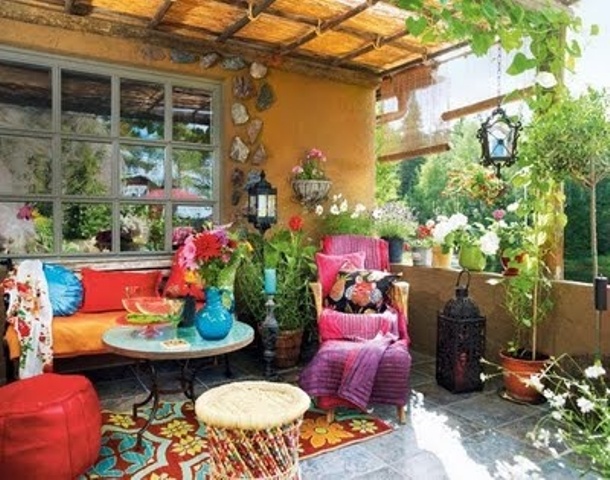 a super colorful boho terrace with a sofa with bold pillows, colorful chairs, stools and a table, lots of greenery and blooms