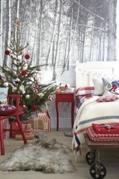 a bright festive bedroom with a mini Christmas tree with red and white ornaments, red furniture, a bench with red blankets and plaid bedding