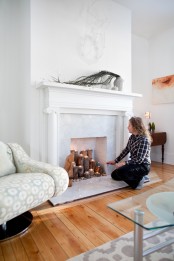 a fireplace with a marble touch and thick tree branches, pebbles and tealights for a natural feel