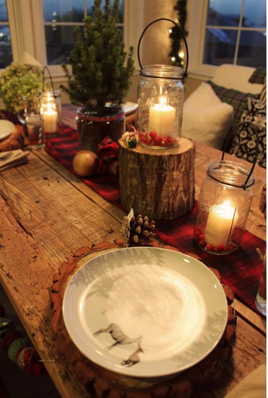 a rustic Christmas tablescape with a red burlap ribbon, candle lanterns, a mini tree and tree stump, wood slice placemats and pinecones all over