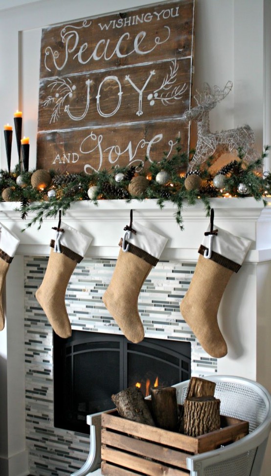 a beautiful rustic Christmas mantel styled with tine balls, silver ornaments, pinecones, evergreens, burlap stockings and a crate with firewood