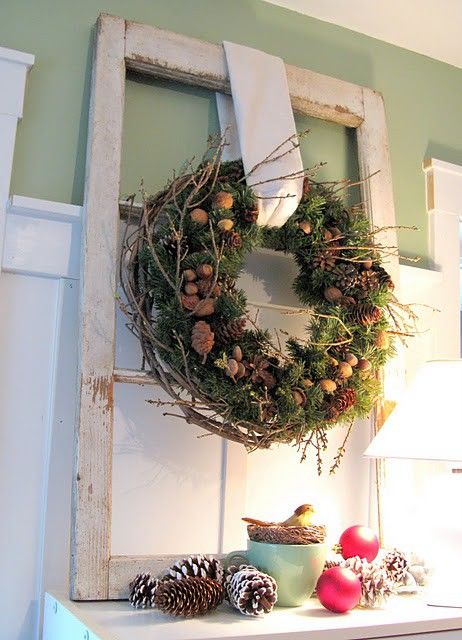 an evergreen Christmas wreath with pinecones, acorns, nuts, twigs, snowy pinecones and ornaments under it on the table for a cozy rustic holiday feel