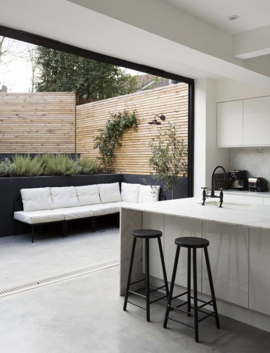 a minimalist neutral kitchen with sleek cabinets and tall stools that can be opened to the small terrace with a garage door