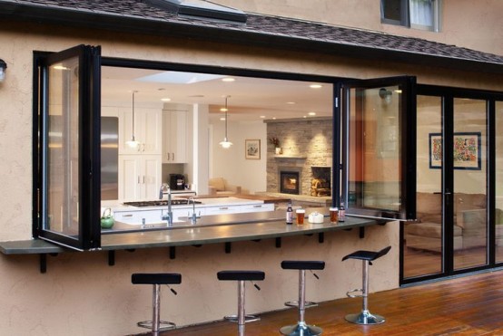 a kitchen with a pass through window and tall stools and a folding window that allow eating outdoors whenever the weather is fine