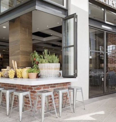 a kitchen with a glazed wall that is a folding window that is a pass through one, with a windowsill and tall metal stools to eat outdoors