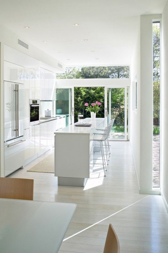 a modern all-white kitchen with a glazed wall with sliding doors that open the kitchen and dining zone to outdoors