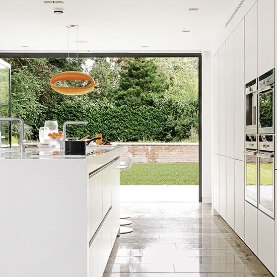 a minimalist white kitchen with a wall that features a garage door to open the kitchen to the garden anytime the weather allows to do so
