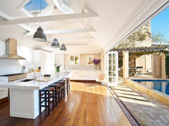 a white farmhouse kitchen with a skylight and a wall with a folding door that opens the space to the pool outdoors is amazing