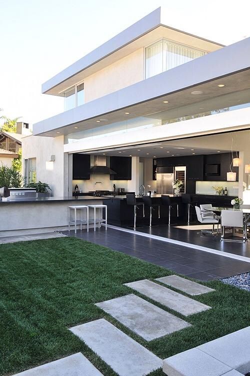 a contemporary black kitchen and a white dining zone with a garage door that opens the spaces to outdoors with an outdoor kitchen that continues the style of the indoor one