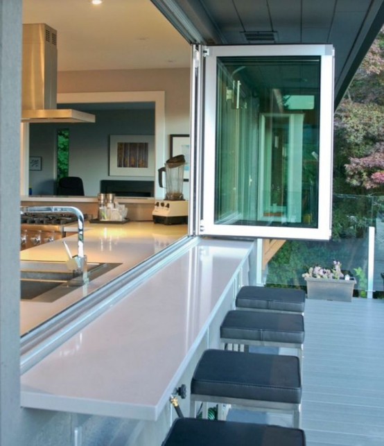 a neutral modern kitchen with a pass through window that is folding and tall stools outdoors for indoor-outdoor meals
