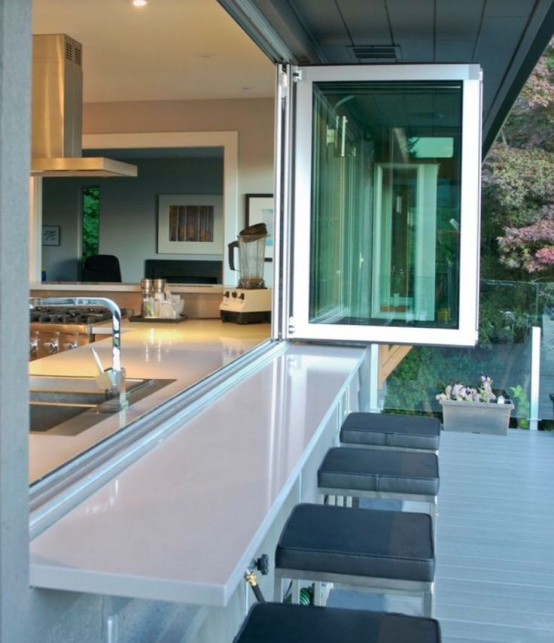 a neutral modern kitchen with a pass through window that is folding and tall stools outdoors for indoor-outdoor meals