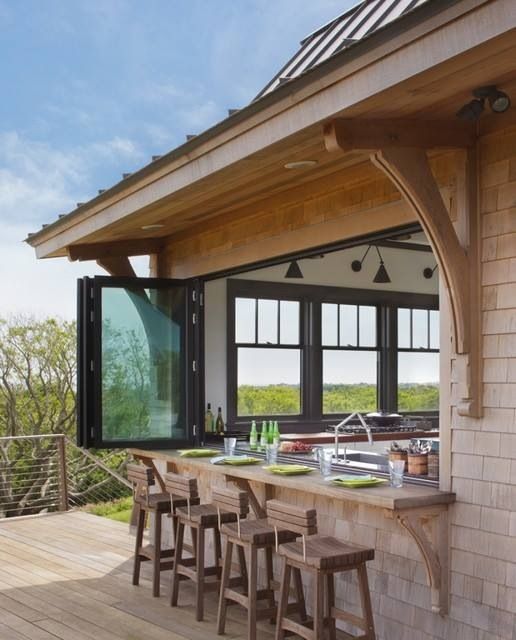 a modern kitchen with white cabinetry and a series of windows including a pass through window that is folding and tall stools at the windowsill