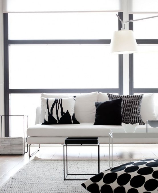 a minimalist black and white living room with a stylish white couch, printed black and white pillows plus coffee tables