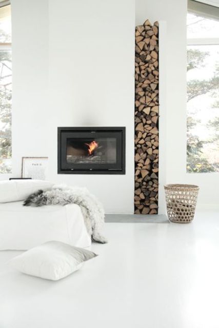 a minimalist all-white living room with a fireplace and a firewood storage space, a white sofa and large windows for more light