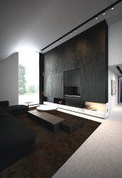 a minimalist living room with a wood clad wall and fireplace, a black sofa and dark stained furniture