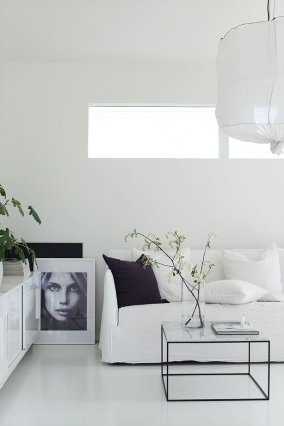 a pure white minimalist living room with a small window, a paper lamp and touches of black for more drama