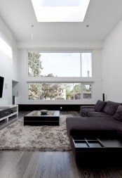 a chic and welcoming minimalist living room with dark furniture, a fluffy rug, a TV and a large window plus a skylight