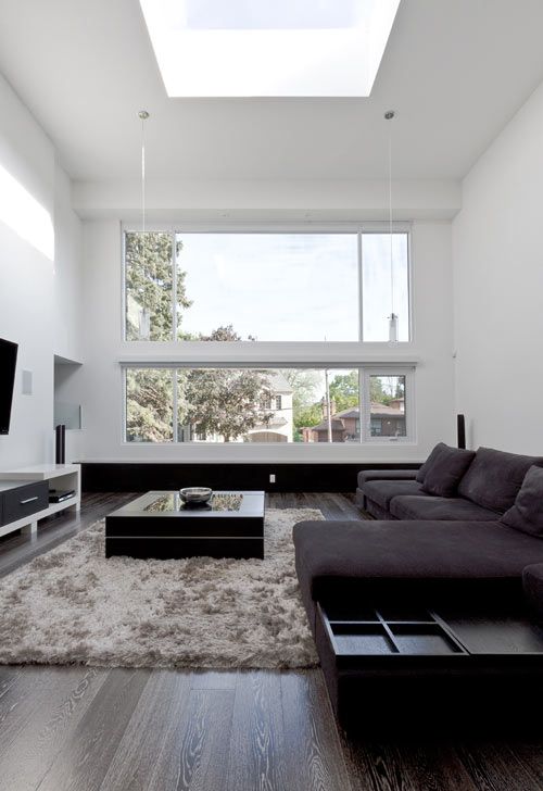 a chic and welcoming minimalist living room with dark furniture, a fluffy rug, a TV and a large window plus a skylight