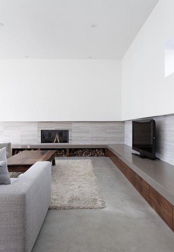 a chic grey and white minimalist living room with a fireplace, firewood storage, grey furniture and a fluffy rug