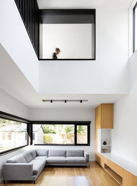 a minimalist double-height living room with a grey sectional sofa, neutral wooden furniture, windows to flood the space with light