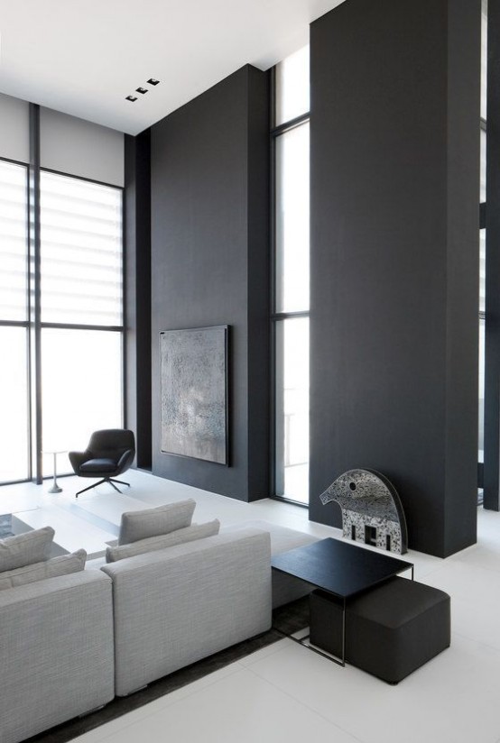 a minimalist living room with black walls, a grey sectional sofa, black furniture items and much natural light