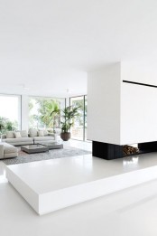 a minimalist and light-filled living room with a fireplace and firewood storage, a grey sectional sofa and panoramic windows
