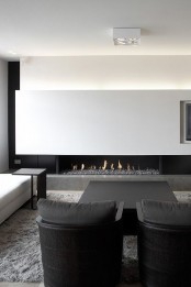 a super elegant black and white minimalist living room with a lit up wall, a fireplace, comfortable black and white furniture