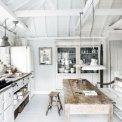 a pure white shabby chic kitchen with whitewashed cabinets, a white fridge, a shabby chic stained dining table and a large whitewashed buffet is cool