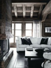 a contemporary meets rustic living room with a hearth, wooden beams on the ceiling and chic black and white furniture
