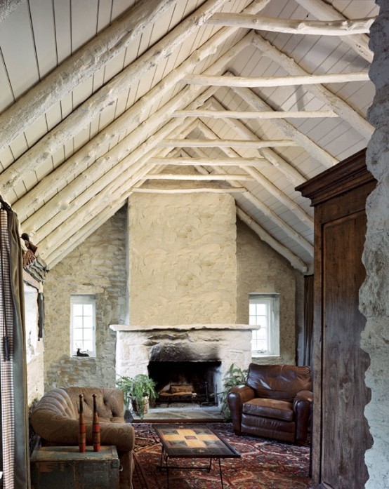 an attic ceiling with beams, a hearth and stone walls make up a cozy rustic backdrop for filling the room