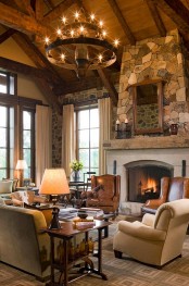 a cabin living room with a stone clad fireplace, a large chandelier, some leather furniture