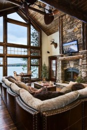a rustic cabin living room with a fireplace clad with stone, an attic ceiling and a double height window plus leather furniture