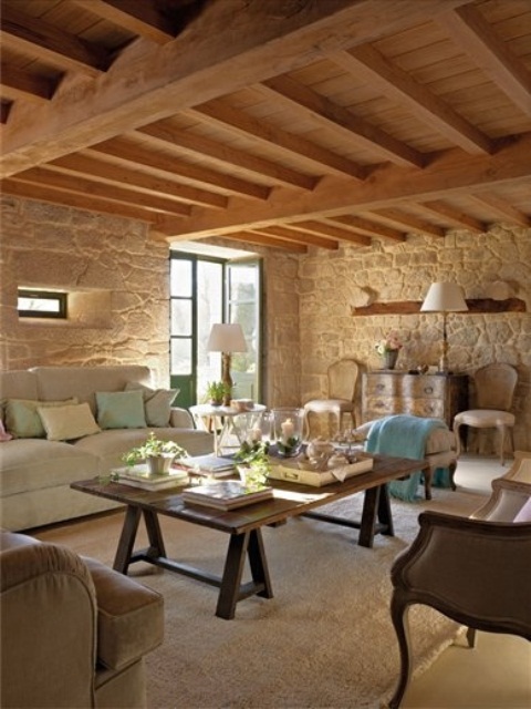 a Provence living room with stone walls, a wooden ceiling wiht beams, rustic furniture and leather sofas