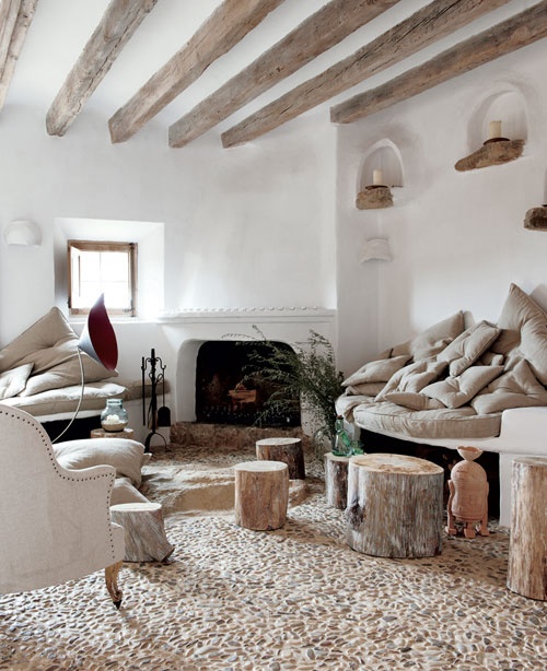 a refined rustic living room with wooden beams on the ceiling, a fireplace, some tree stump stools and chic furniture