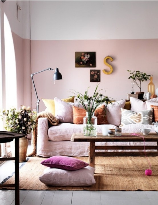 a beautiful and relaxed feminine living room with color block walls with pink, a pink sofa with colorful and printed pillows, artworks, blooms and greenery and a rust-colored rug