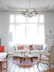 a delicate living room in neutrals, with vintage touches – white seating furniture, pink and coral pillows and a chic vintage chandelier