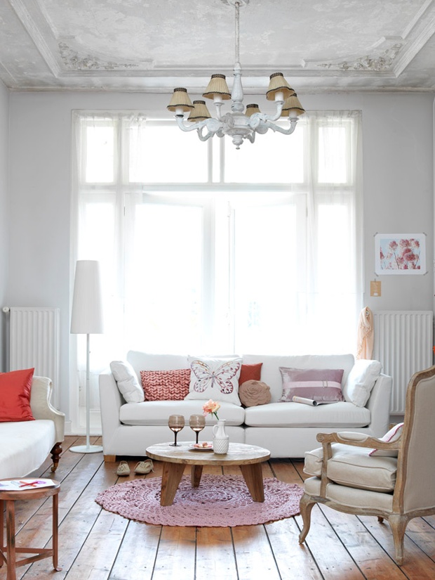 a delicate living room in neutrals, with vintage touches   white seating furniture, pink and coral pillows and a chic vintage chandelier