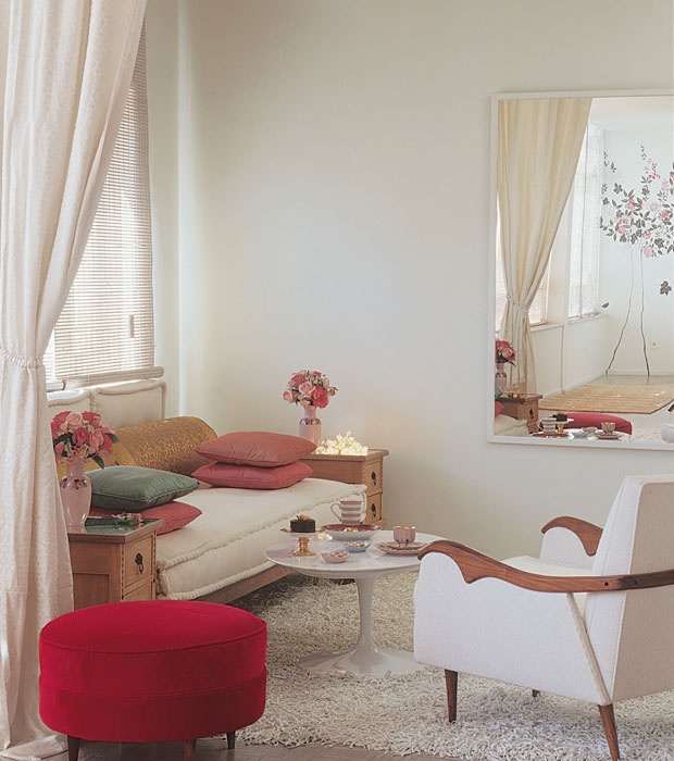 a pretty and elegant neutral living room with a vintage sofa, a chic white chair, a red pouf and a mirror plus some blooms