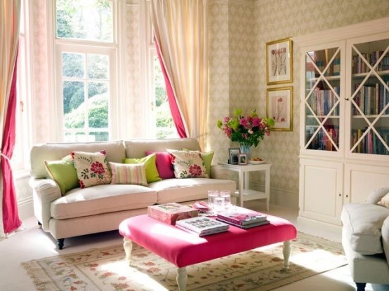 a chic modern feminine living room done in neutrals, with a white sofa, a hot pink ottoman, matching curtains, printed wallpaper and a rug and some bold blooms