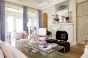 a vintage-inspired feminine living room with a large fireplace, white seating furniture, lilac curtains, a glass coffee table and pink pillows